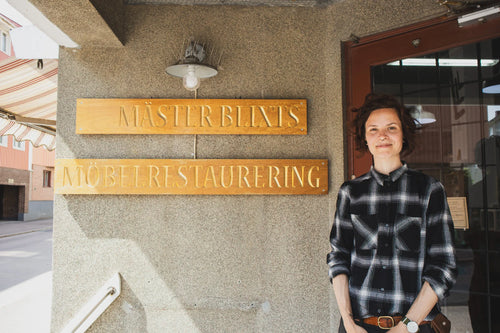 Pernilla Blixt in front of the Mäster Blixt Möbelrestaurering sign