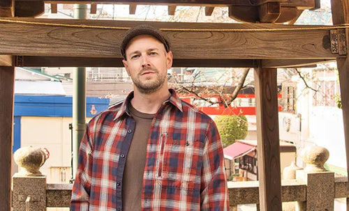 Daniel in a plaid shirt in front of a wooden structure