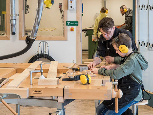 Pupils wearing ear protection at workbenches in a woodwork room